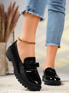 Close-up view of glossy black patent leather loafers featuring a gold chunky chain anklet detail