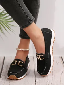 Detail view of black platform loafers with gold metal chain buckle and white sole
