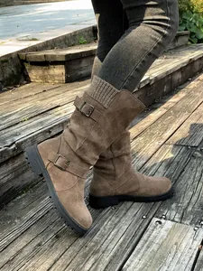Detail shot of brown suede mid-calf boots with knit collar and decorative buckles on stairs