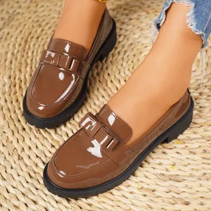 Detailed view of women's brown patent leather loafers featuring thick soles and a bow accent