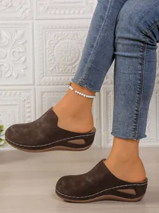 Close-up of brown suede wedge mules with contrast stitching and decorative cutout sole