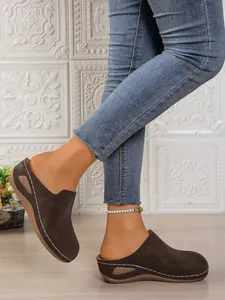 Close-up of brown platform wedge mules featuring white hand-stitched detail on a model's feet