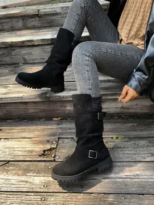Detail of black suede mid-calf boots with buckle straps and knit collars on wooden steps