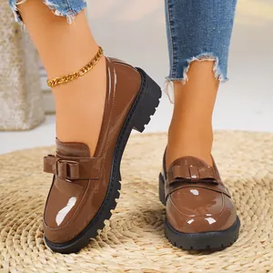 Glossy brown patent leather loafers with bow detail and chunky sole on straw mat.
