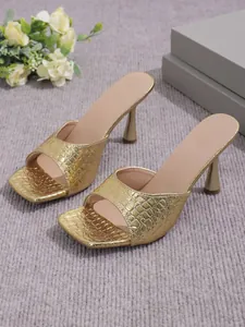Detailed view of gold square-toe mule sandals featuring textured stone pattern and slim heels
