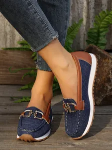 Close-up of casual denim loafers with gold metal buckle and brown leather trim.