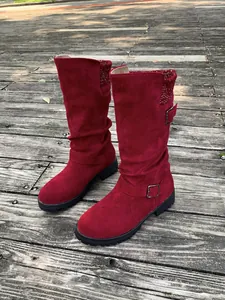 Detail view of wine red suede mid-calf boots with knit trim and buckle on wood floor.