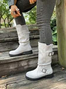 Detail of off-white suede western boots with belt buckles and knit collars on stairs