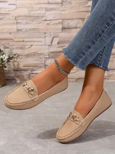 Close-up view of beige faux leather loafers with decorative gold metal buckle on feet.