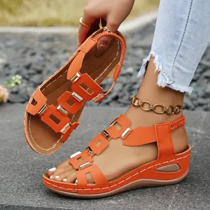 Close-up of vibrant orange wedge sandals with gold metal buckle accents and elastic strap.