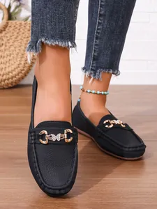 Close-up of women's black loafers featuring a golden butterfly buckle on wooden floor