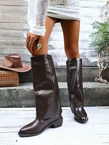 Dark brown pointed-toe wide-leg boots with thick mid-heels in a rustic outdoor setting.