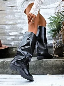 Detail view of black slouchy sleeve boots with pointed toe and chunky heel on rustic steps.