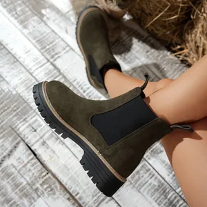 Botas Chelsea de gamuza verde oliva con suelas de plataforma sobre suelo de madera blanca