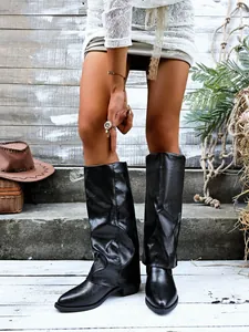 Detailed view of black pointed toe pant leg boots with chunky heels on a model.