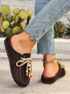 Side view of brown suede mules featuring bohemian beaded laces and white stitching
