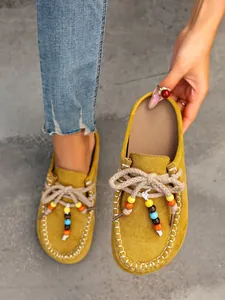 Close-up of yellow suede mule slippers with colorful beads and thick rope laces.