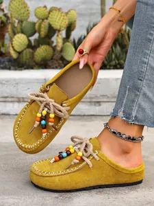 Close-up of mustard yellow suede platform mules with colorful beads and braided laces