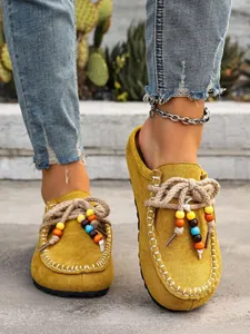 Close-up detail of yellow suede mules featuring colorful beaded laces and moc-toe stitching