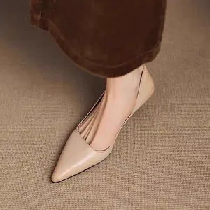 Detailed side view of elegant beige pointed-toe pumps worn with brown trousers