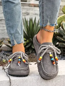 Detailed view of grey suede platform mules with colorful bead and rope accents.