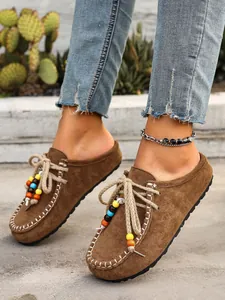 Macro detail shot of brown suede mules with colorful beaded laces on concrete floor