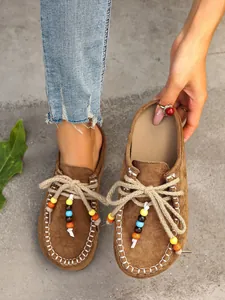 Close-up of brown suede platform mules featuring decorative beads and rope ties.