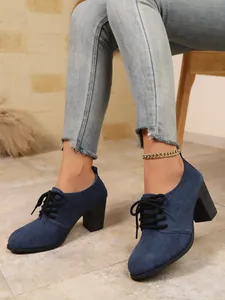 Seitenansicht von dunkelblauen Wildleder-Schnürschuhen mit hohem Absatz und Jeans.