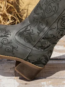 Close-up of grey western knight boots with black embroidery and chunky wooden-look heel.