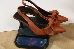 Detailed view of brown pointed toe bow slingback pumps on a digital scale weighing 358.2g