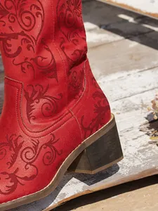 Detail shot of a red western boot with intricate floral embroidery on a wooden deck