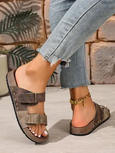 Detail of brown rivet Birkenstock-style sandals with buckle straps on model's feet