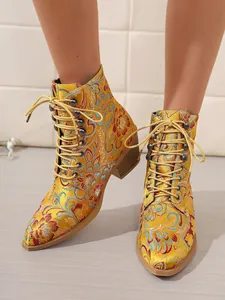 Detailansicht der gelben Satin-Stiefeletten mit bunter Blumenstickerei und Schnürung.