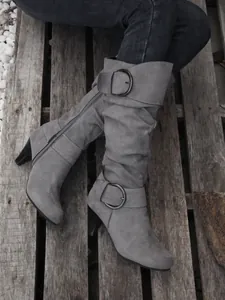 Stylish grey faux suede slouchy high-heeled boots featuring decorative buckles on wood background
