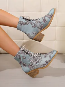 Detail von hellblauen Satin-Stiefeletten mit Vintage-Stickerei und Blockabsatz.