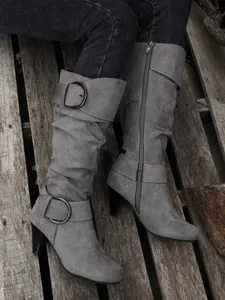 Side view of grey slouchy knee-high boots with buckles and high heels on wood