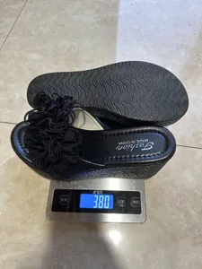 Detail of black wedge platform sandals with flower decor shown on a weighing scale