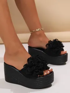 Close-up view of elegant black wedge platform sandals featuring large 3D floral decorations