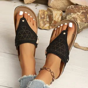 Close-up view of black retro flat thong sandals with laser-cut patterns on feet.