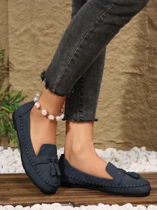 Detail view of navy blue flat loafers with decorative tassels and hand-stitched edging