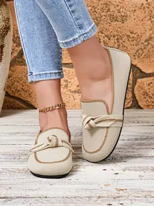 Detailopname van beige fly-knit loafers met een decoratieve knoop en contrasterende biezen