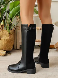 Close-up of black British style knee-high boots with side zipper and belt buckle detail