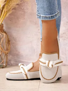 Close-up van witte gebreide loafers voor dames met gedraaid knoopdetail aan de voet.