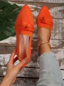 Detail of bright orange pointed-toe fly-knit flat shoes featuring a stylish knot design