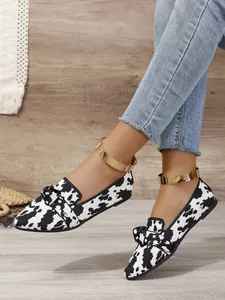 Close-up detail of cow print flyknit loafers with bow accent and pointed toe design.