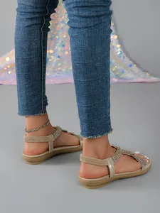 Detail view of women's gold flat sandals with shimmering rhinestones and elastic straps.