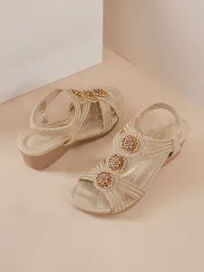 Detail of gold wedge sandals with rhinestone floral embellishments and elastic strap