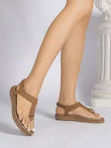 Vista detallada de sandalias planas de estilo bohemio marrón con tira en T en los pies