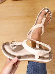 Detalle de sandalias planas color crema con detalles dorados y correa elástica.