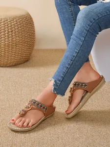 Close-up view of elegant Bohemian flat sandals with floral rhinestones worn with blue jeans